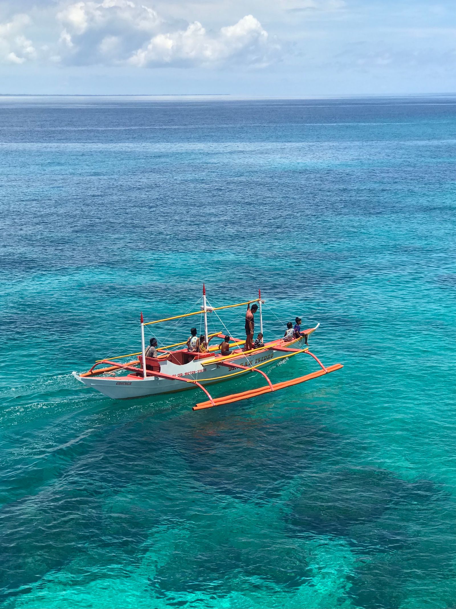 Perahu bercadik dengan penumpang di laut biru jernih